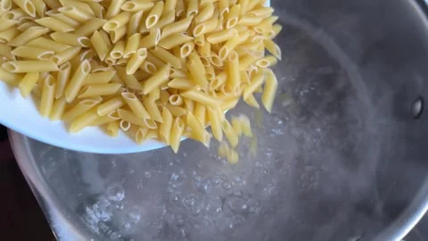 Loading raw tubular pasta penne into boiling water for preparing Stock Footage 323857440