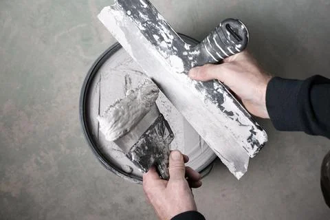 Loading wall filler onto taping knife using putty knife over plaster bucket Stock-Fotos
