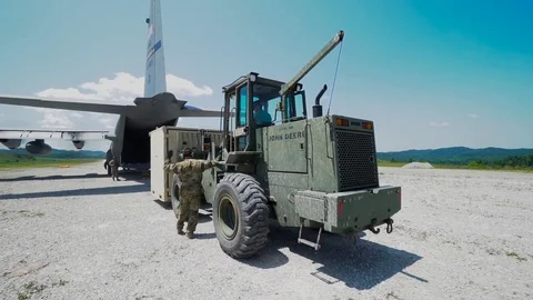 Loadmaster guiding forklift truck operator loading steel container onto C-130 Stock Footage 113610586