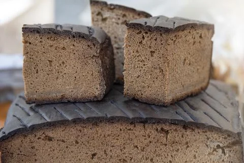 A loaf of black rye bread on the counter of a bakery is cut into pieces, close Stock Photos