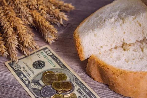 A loaf of bread and ears of ripe wheat lie on a wooden table next to US dolla Stock Photos