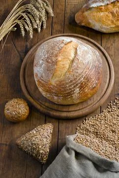 Loaf of bread and grain of wheat on wooden table Stock Photos