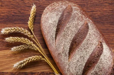 Loaf of bread and wheat over wooden background Stock Photos