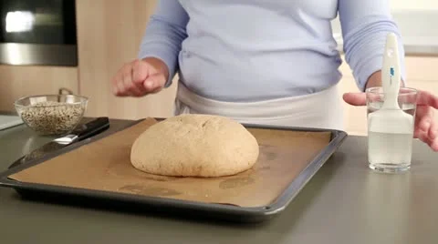 A loaf of bread being brushed with water, scored and sprinkled with sunflower Stock Footage 24672975