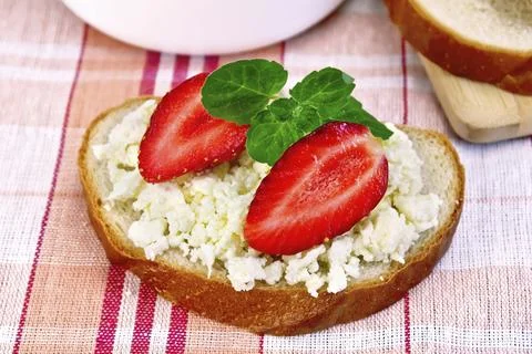 A loaf of bread with curd cream, mint and strawberries, a bowl of cottage Stock Photos