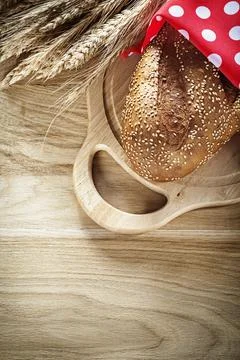 Loaf of bread rye ears red dotted fabric cutting board on wooden background Stock Photos