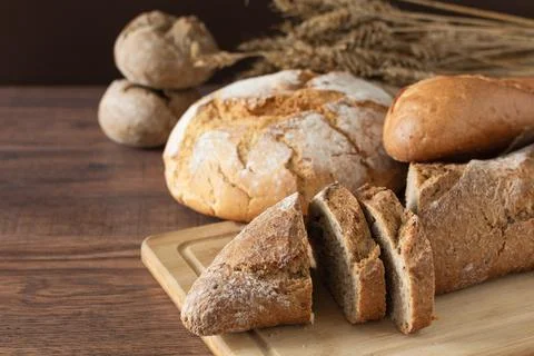 Loaf of bread sliced and other variety of bread on wooden table. Stock Photos