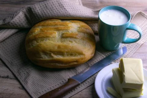 A loaf of bread under a towel on the table with a glass of milk and butter Stock Photos