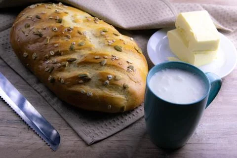 A loaf of bread under a towel on the table with a glass of milk and butter Stock Photos