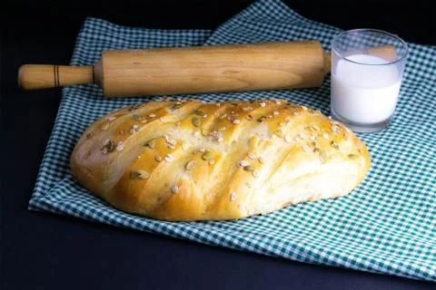 A loaf of bread under a towel on the table with a glass of milk and butter Stock Photos