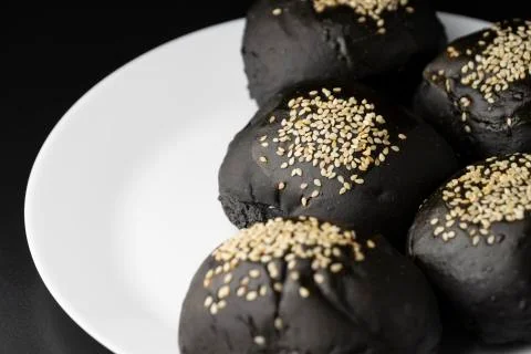 Loaf of charcoal bread bun with white sesame on top in the white plate Stock Photos
