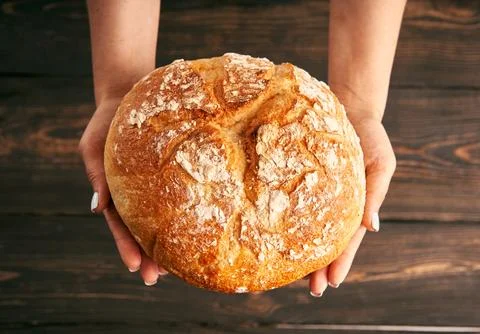 Loaf of fresh made white bread in woman hands on wooden table background Stock-Fotos