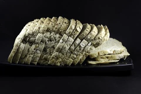 Loaf of multigrain bread on black platter isolated on black background. sli.. Stock Photos