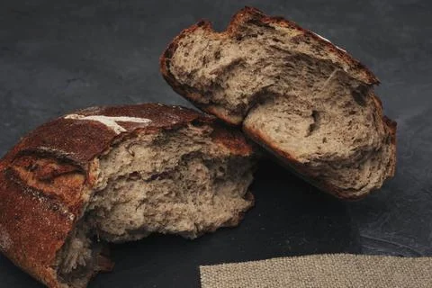 A loaf of round warm bread broken in half. Freshly baked dark grain bread, br Stock Photos