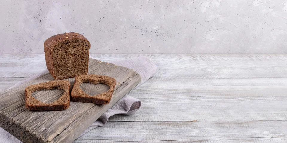 Loaf of rye bread and two slices with carved holes of heart shape in them o.. Stock Photos