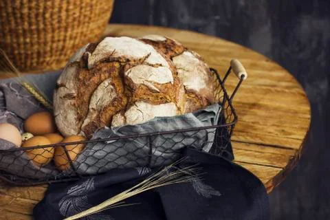 Loaf of rye bread in a basket with chicken eggs on the table Stock Photos