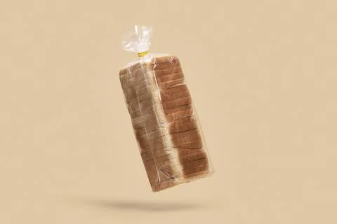 Loaf of sliced bread in clear plastic bag floating against peach background Stock Photos