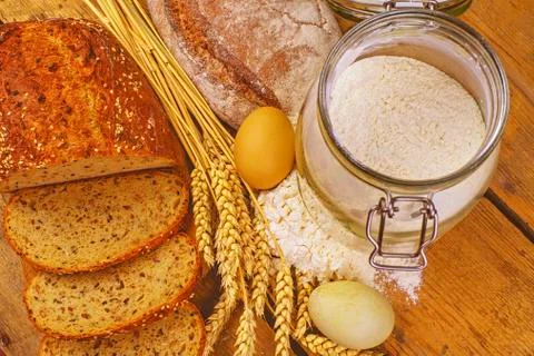 Loafs of bread, slices of bread, wheat flour, eggs and ears of grain on wood  Stock-Fotos
