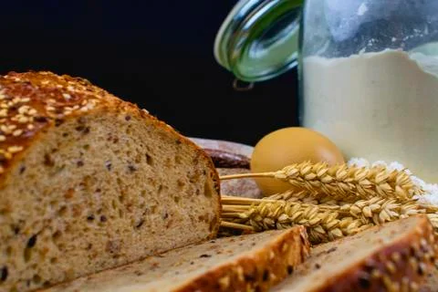 Loafs of bread, slices of bread, wheat flour, eggs and ears of grain on wood  Stock-Fotos