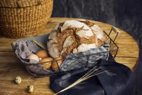 Loafs of rye bread in a basket with chicken eggs on the table Stock Photos
