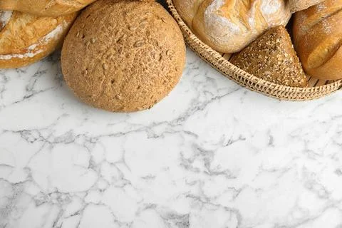 Loaves of different breads on white marble background, flat lay. Space for te Foto stock