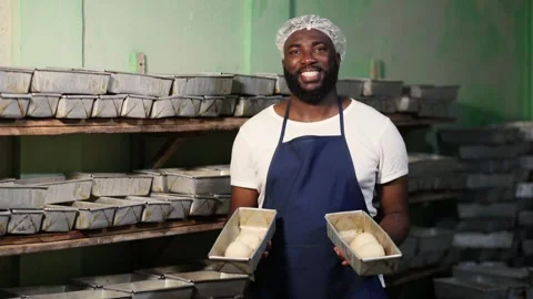 Local African baker holds fresh bread dough in pans for oven, proud SME owner Stock-Footage 346565293