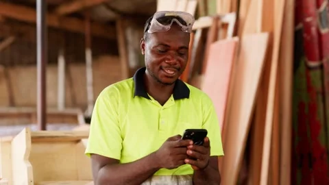 Local African male carpenter using smartphone in his workshop Stock Footage 346733926
