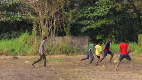 Local kids of Kerala playing football from a dry grass field Stock Footage