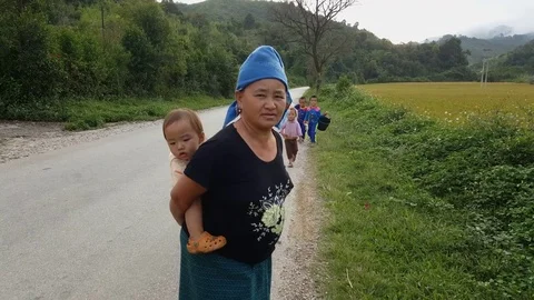 Local Laos woman with baby on back and young children, road, rural Houhaphan Stock Footage