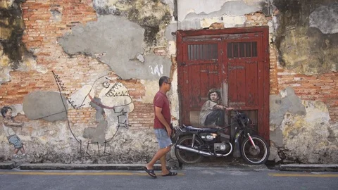 Local man strolling past one of George Town's famous street art displays. Stock Footage 77424290
