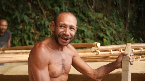 Local papuan man with red teeth from chewing a betel is building a boat. PNG Vídeos de archivo 310859340