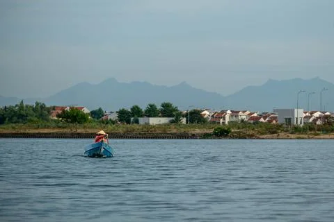Local Resident in Conical Hat Rowing a Small Blue Boat Across a Wide River Stock Photos