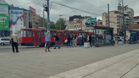 Locals wait at a bus stop in central Belgrade, Serbia, as an old red tram 스톡 동영상 314480142