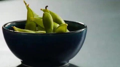 Lock down shot of salt being sprinkled on hot Edamame Stock Footage 98247777