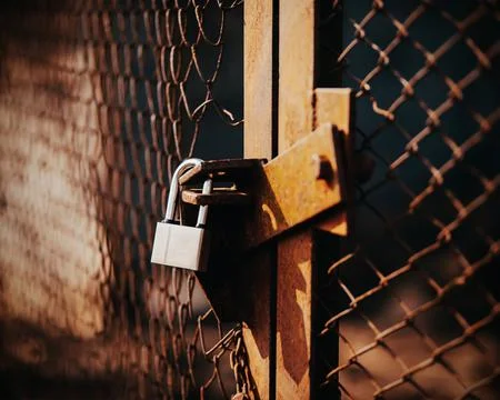 A lock hangs on the old rusty mesh broken gate, closing them, illuminated by  Stock Photos