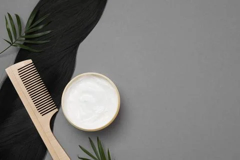 Lock of healthy black hair, comb and cosmetic product on grey background, fla Stock Photos