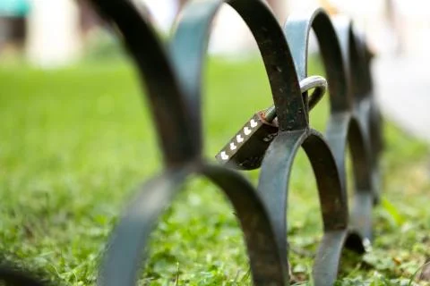 Lock with hearts on fence beside grass field in public park. Stock Photos