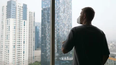 Lockdown and social isolation concept. Lonely man in a face mask looking at the Stock Footage 156191284