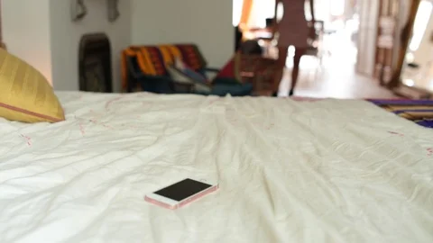 Lockdown mid section of woman walking towards smart phone on bed Stock Footage 114860515