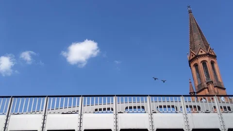 Lockdown shot of birds flying over the train bridge in front of the church Vídeo Stock 114880284