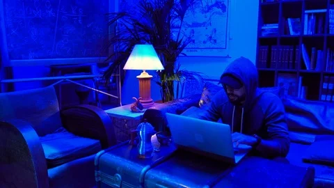 Lockdown shot of a man working on laptop in a blue lit room Stock Footage 114885276