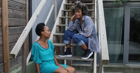 Lockdown shot of two female friends talking and smiling while sitting on steps Stock Footage 120088488