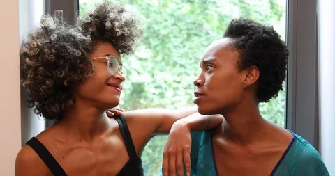 Lockdown shot of two friends talking and smiling while sitting near window Stock Footage 120126520