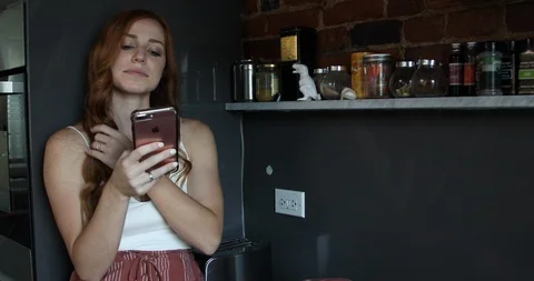 Lockdown shot of woman using smartphone while standing in kitchen Stock Footage 119976867