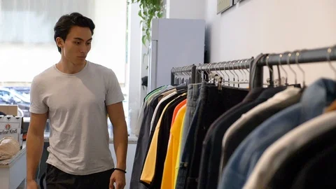 Lockdown shot of young Asian man checking clothes in clothes shop Video stock 114874635