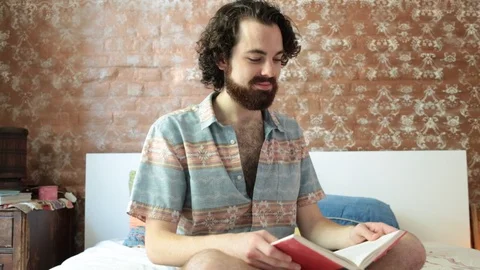 Lockdown shot of young man reading book on bed and smiling at home Stock Footage 114859509