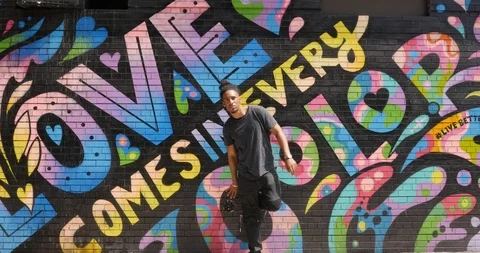 Lockdown shot of young man standing against wall with colourful graffiti Stock Footage 120063408