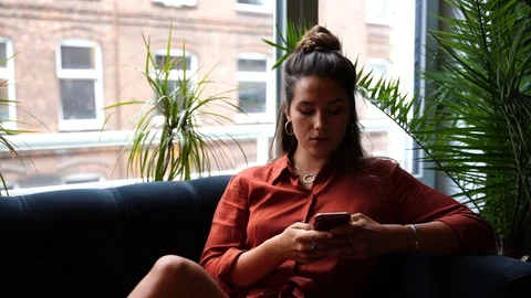 Lockdown shot of young woman using smartphone while sitting on sofa Stock Footage 114883507