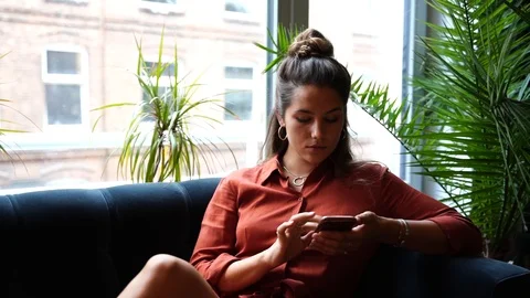 Lockdown shot of young woman using smartphone while sitting on sofa Vídeo Stock 114883510