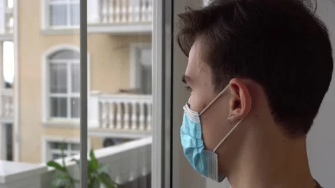 Lockdown, Stay-at-home order. A man in medical masks sad looks in the window Stock Footage 147704052